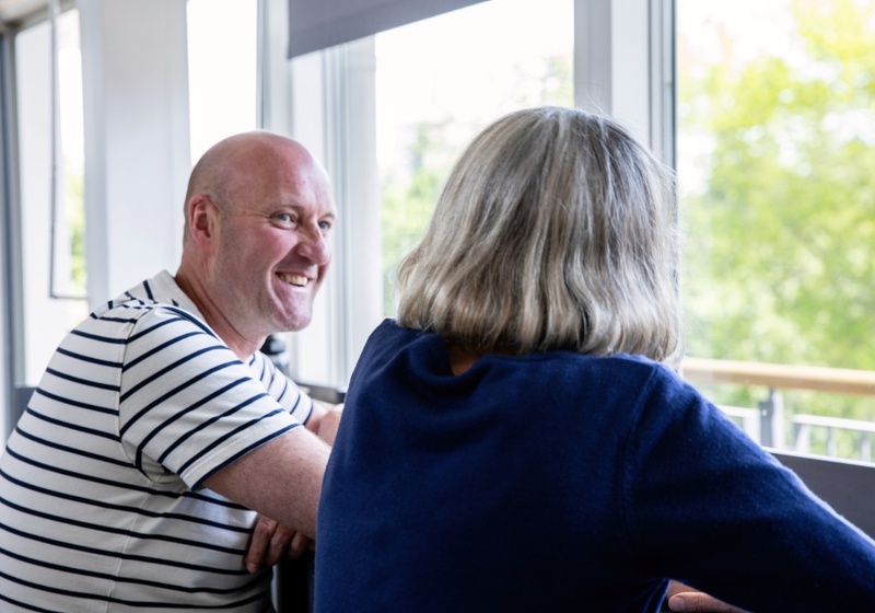 Man in striped shirt smiling, talking to woman.